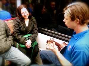 Christopher Scott plays on the W Light Rail Line as Molly Jenkins listens intently.